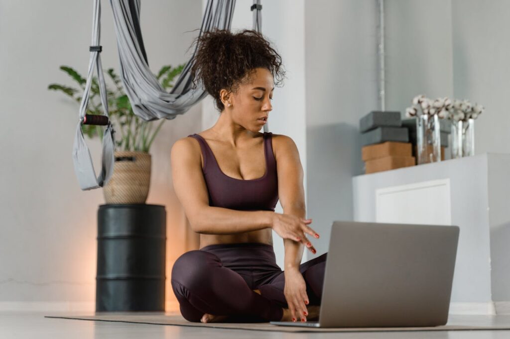 A woman in yoga attire uses a laptop for meditation in an indoor setting, promoting digital wellness.
